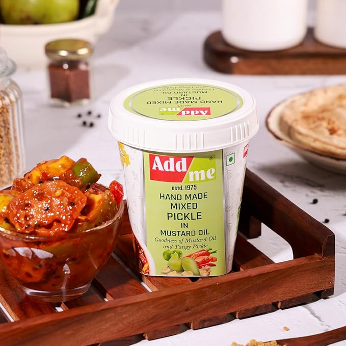Add me hand made mixed pickle in mustard oil on a wooden tray with a bowl of pickle and spices in the background.