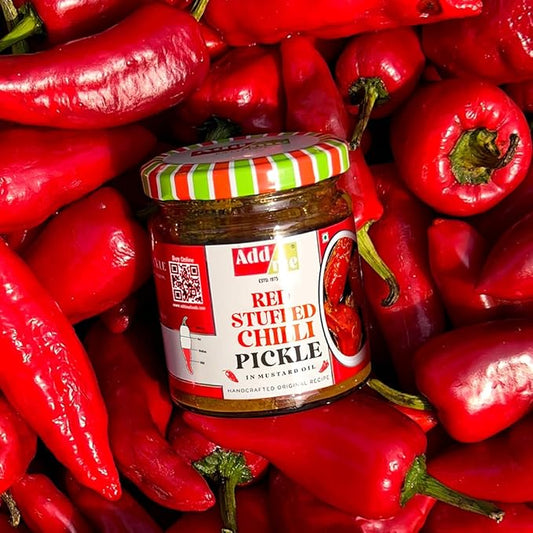 Jar of red stuffed chili pickle surrounded by red peppers