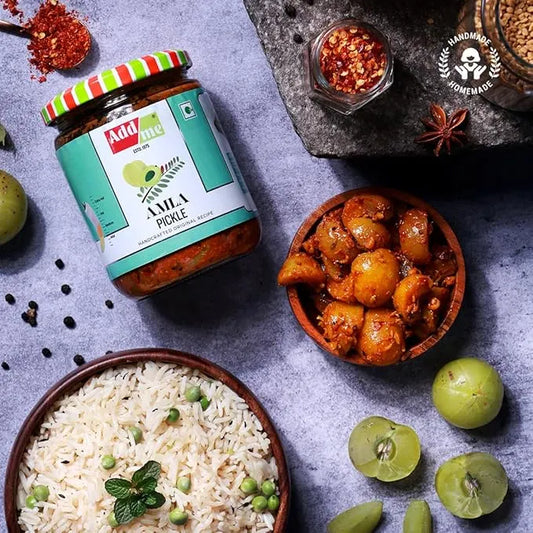 Jar of Amla pickle with a bowl of rice and a bowl of pickled amla on a gray surface. Seedless Amla Pickle