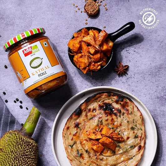 Jar of Mirchi Masala pickles with a bowl of fried food and a flatbread on a gray surface.
