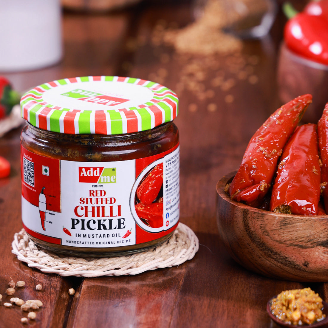 Add Me Foods: Jar of red stuffed chilli pickle with a striped lid on a wooden surface