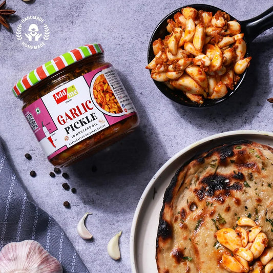 Jar of garlic pickle with a dish of pasta and flatbread on a gray surface.