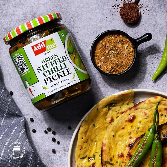 Jar of 'Add me' green stuffed chilli pickle with a side of flatbread and chilies on a gray surface.