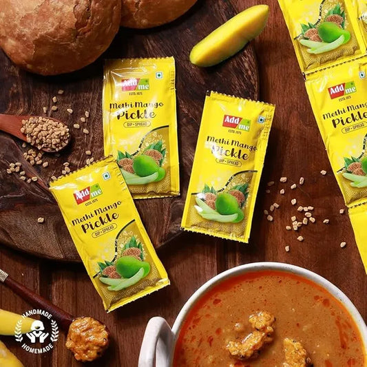 Add Me Foods: Add me Mehi Mango Pickle packets on a wooden surface with a bowl of soup and ingredients.