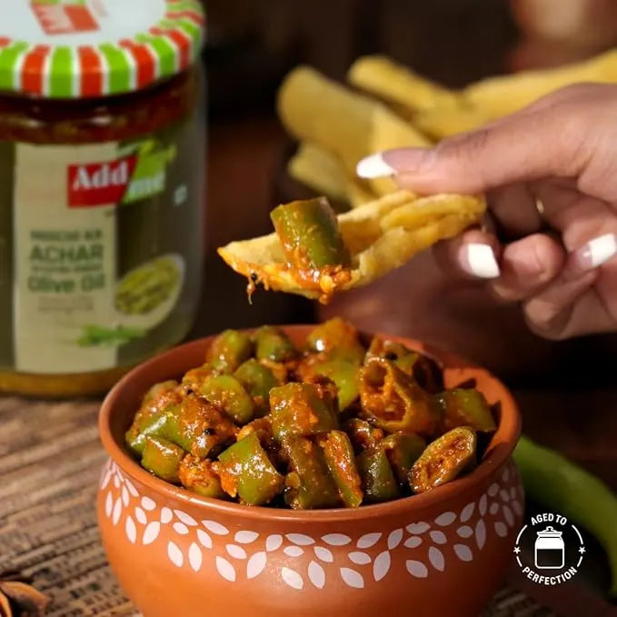 Person dipping a chip into a bowl of green bean dish with a jar of Add me Achar in the background.