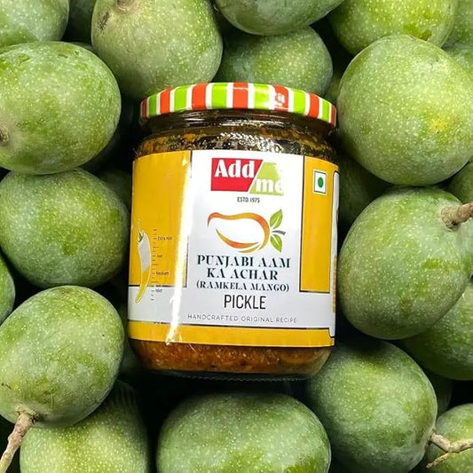 Jar of Adda Punjabi Aam Ka Achar pickle surrounded by green mangoes