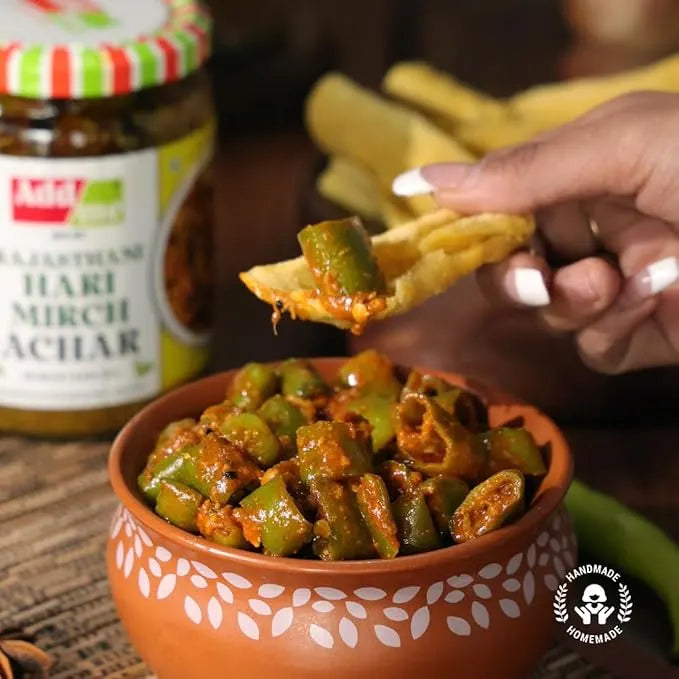 Add Me Foods: Person dipping a chip into a bowl of green chilies with a jar of Aashirwad Mirch Achar in the background.