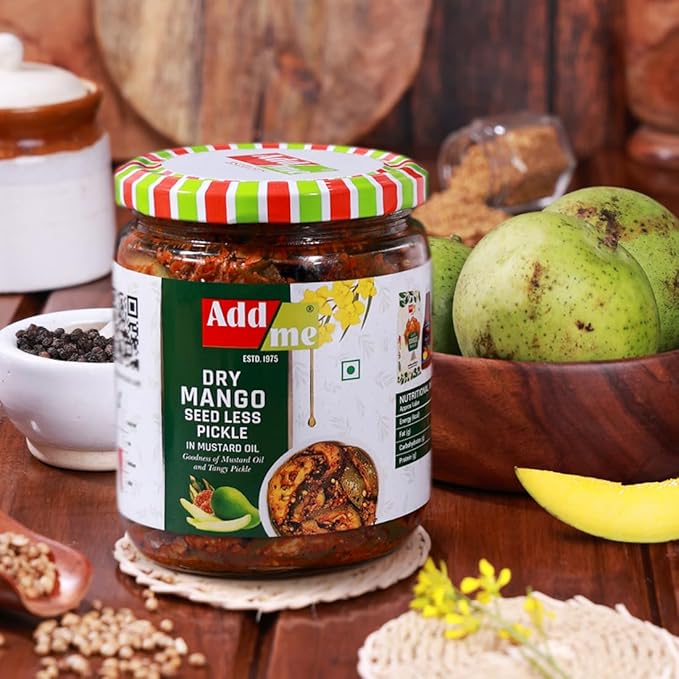 Jar of Add Some Dry Mango Seed Less Pickle on a wooden table with mangoes and spices.