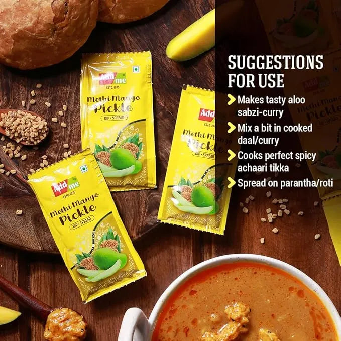 Yellow packets of Methi Mango Pickle on a wooden surface with a bowl of curry and bread.