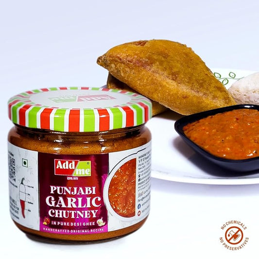 Jar of Punjabi Garlic Chutney with a striped lid, next to a bowl of chutney and bread on a white background.