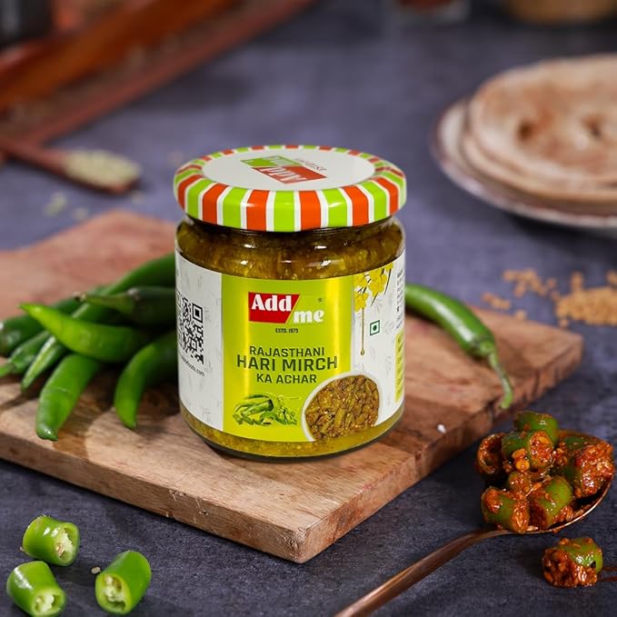 Jar of Add Me Rajasthani Hari Mirch Ka Achar with green chilies and a spoonful of chutney on a wooden board.