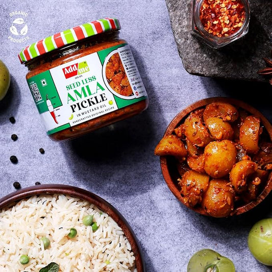 Jar of Add Vite Seedless Amla Pickle with a bowl of pickles and rice on a gray surface.
