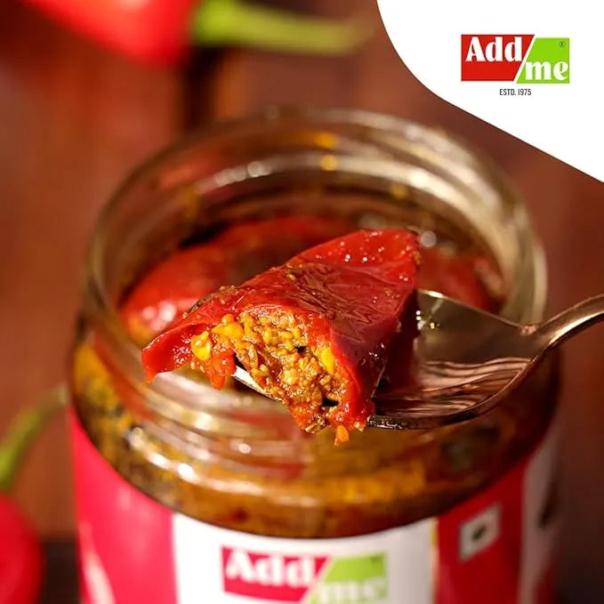 Spoon with stuffed red pepper over a jar of Add Me brand food on a wooden surface. chilli pickle