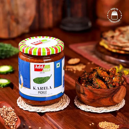 Jar of Add Me Karela Pickle on a wooden table with ingredients and a bowl of pickled vegetables.