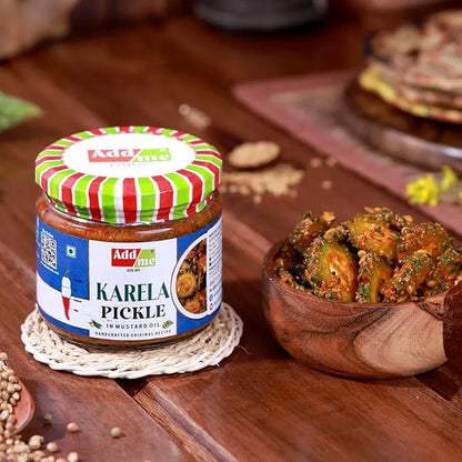Jar of Adda Me Karela Pickle on a wooden surface with a bowl of pickles.