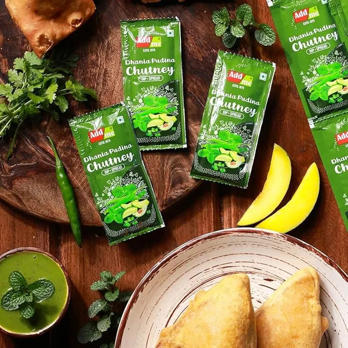 Green packets of Dhanva Chutney on a wooden surface with ingredients and food items.