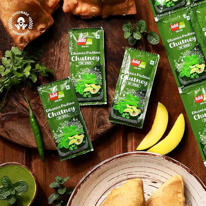 Add Me Foods: Green packets of Dhania Pidina Chutney on a wooden surface with food items.