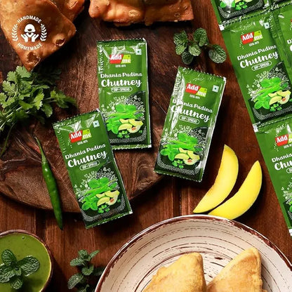 Add Me Foods: Green packets of Dhania Pidina Chutney on a wooden surface with food items.