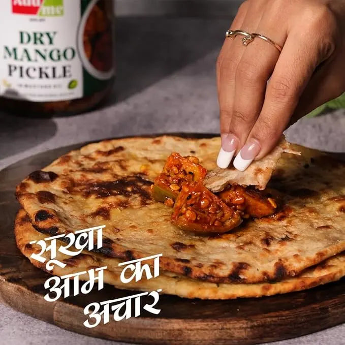 Person dipping a piece of naan into a bowl of curry with a bottle of dry mango pickle in the background. mango pickle, chilli pickle