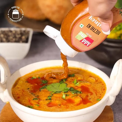 Hand pouring a red sauce from a bottle into a bowl of soup with a blurred background