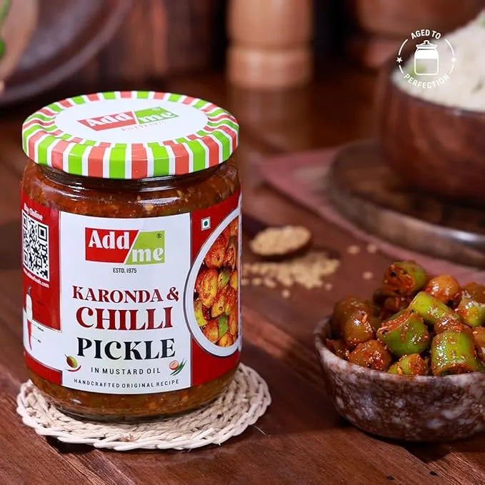 Jar of Add Me Karonda & Chilli Pickle on a wooden surface with a bowl of pickles.