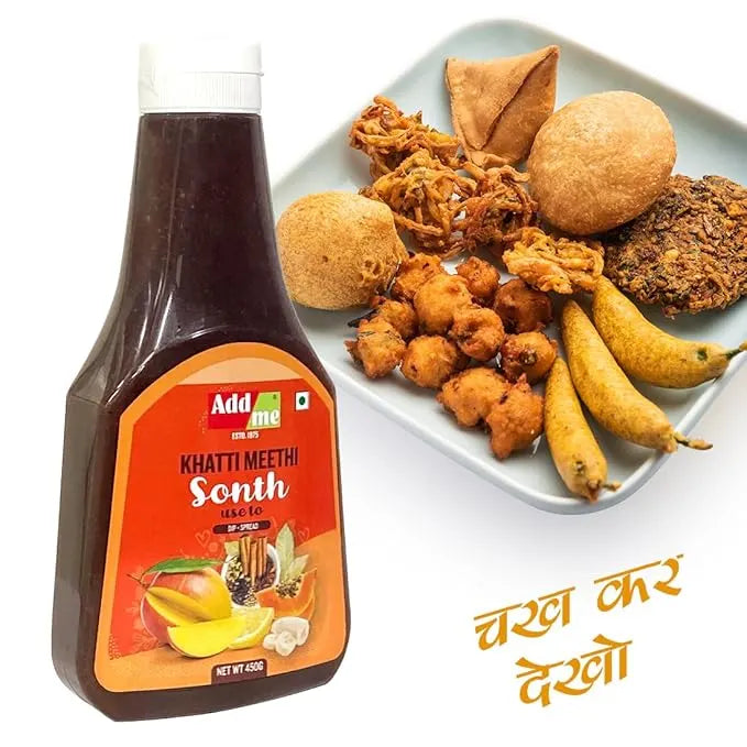 Bottle of Add Me Khatti Meethi Sonth with a plate of fried snacks and fruits on a white background