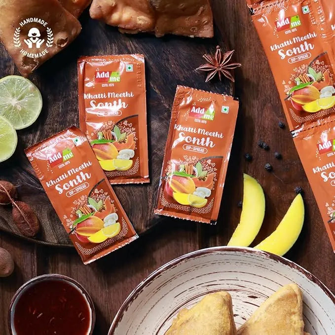 Add Mi Khatti Meethi Sonth packets on a wooden surface with ingredients and a bowl of samosas.