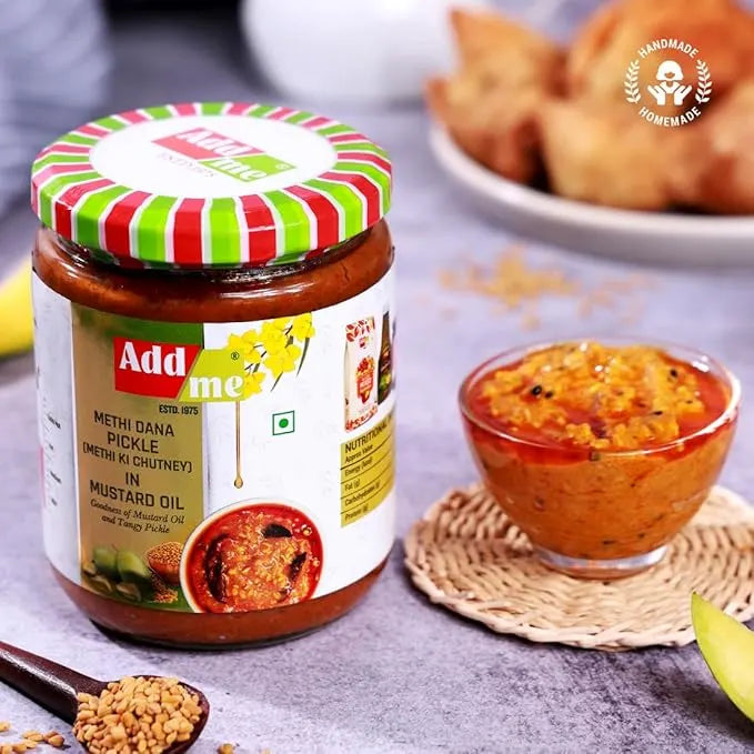 Jar of Add Me Methi Dana Pickle with a striped lid, bowl of pickle, and snacks on a table.