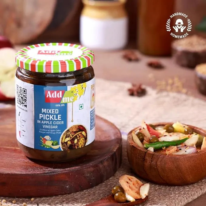 Jar of 'Add me' mixed pickle with a colorful lid on a wooden surface, surrounded by ingredients.