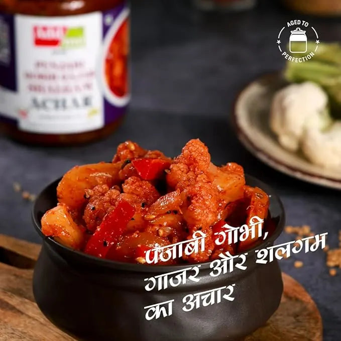 Spicy dish in a black bowl with a bottle of pickle in the background