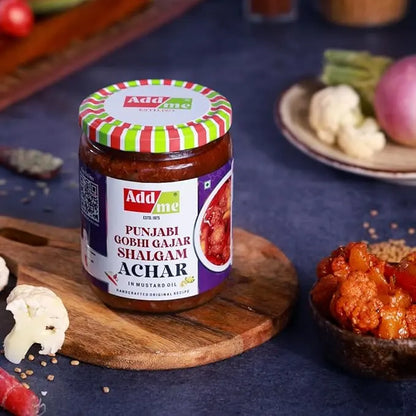 Jar of Adda Me Punjabi Gobhi Gajar Shalgam Achar on a wooden board with ingredients in the background.