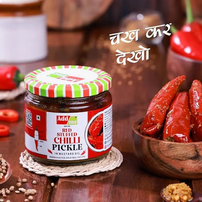 Jar of red sieved chilli pickle with a bowl of red chilies on a wooden surface.