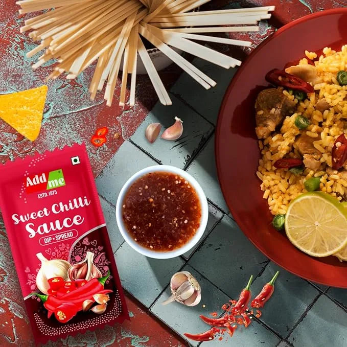Add Me Foods: Add me Sweet Chilli Sauce packet with a dish of rice and vegetables, noodles, and lemon on a textured surface.