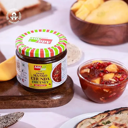 Jar of Adda Sweet Mango Chunda Chutney with a bowl of chutney and snacks on a table.