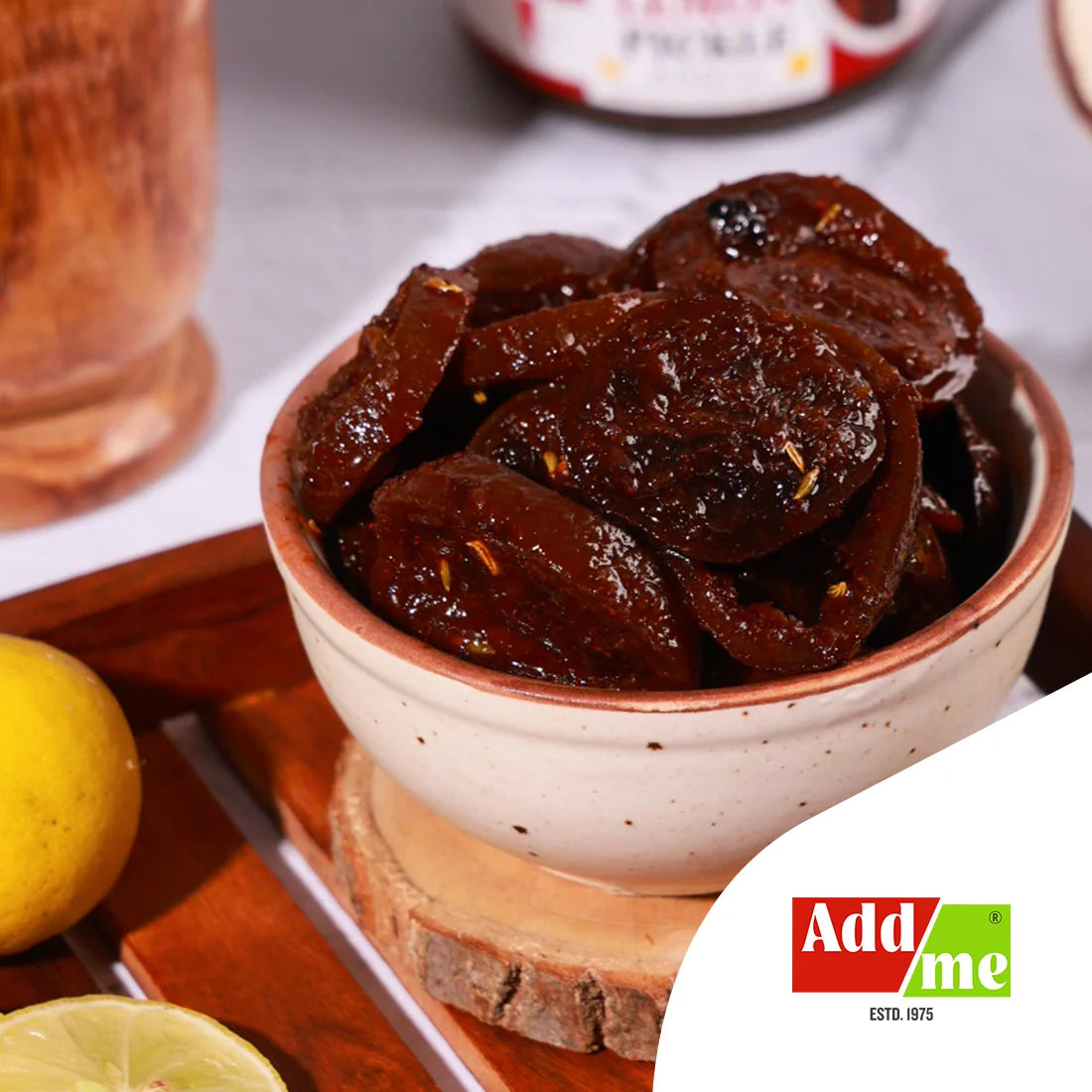 Dried fruit slices in a bowl with a lemon and a glass of juice on a wooden coaster, featuring the Add Me brand. lemon pickle